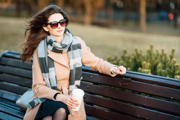 Portrait young smiling European woman walking along city street with takeaway coffee in her hands, beautiful girl resting outdoors