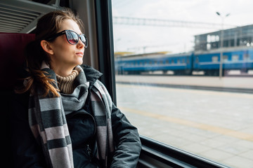 Obraz premium Young woman wearing travel glasses, looking out the window, sitting in train