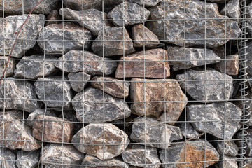 A pile of granite rocks in a metal cage used for flood prevention, mostly grey in colour