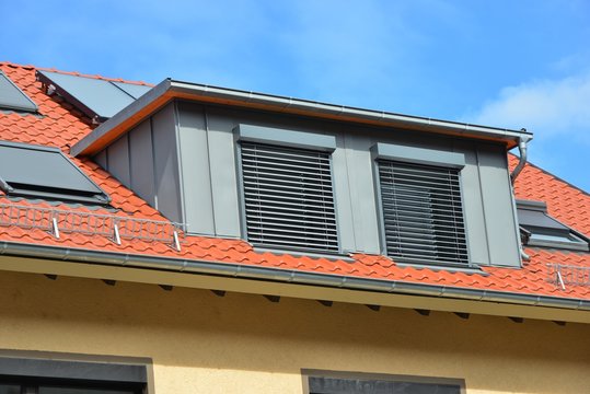 Mit Stehfalz-Metall verblendete Schleppgaube mit Außen-Rollladen auf Ziegeldach mit Dachfenstern, Solaranlage, Dachrinnen und Schneefang