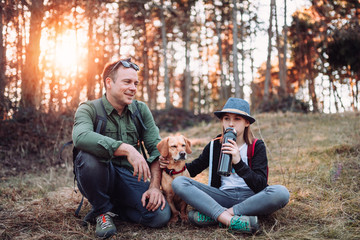 Teenage girl drinking water in forest with her father and dog