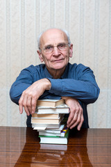 elderly man with glasses folded his cross on the cross hands on a stack of books