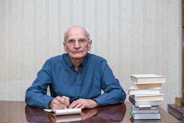 an elderly man in a blue shirt is sitting at a table with books, a pen and a notebook