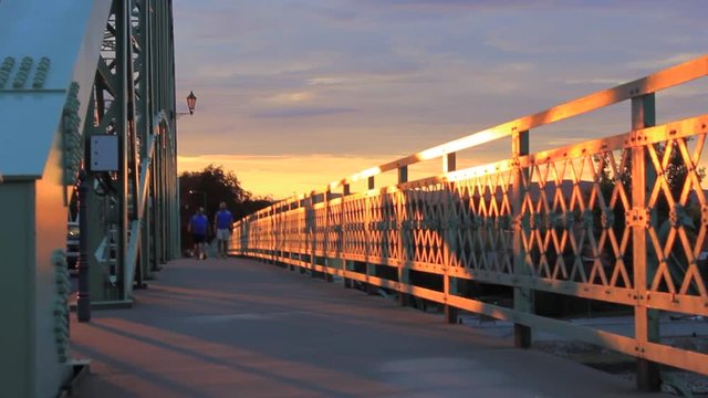 Two people walking slowly on M&aacute;ria Val&eacute;ria Bridge in Hungary, Europe. The sun is slowly setting.