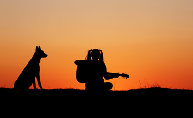 Fototapeta na wymiar Silhouette girl guitarist on sunset background, silhouette of a dog breed Belgian Shepherd Malinois, happy friends, outdoor