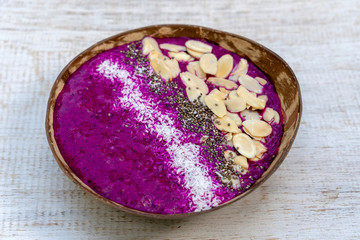 Red smoothie in coconut bowl with dragon fruit, avocado, almond flakes, coconut chips and chia seeds for breakfast , close up. The concept of healthy eating, superfood