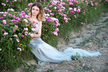 Beautiful girl  in grey dress relaxed in roses garden.