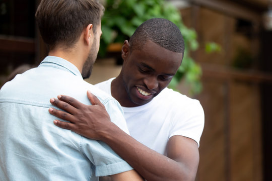 Happy two multiracial male best friends greeting embracing at meeting
