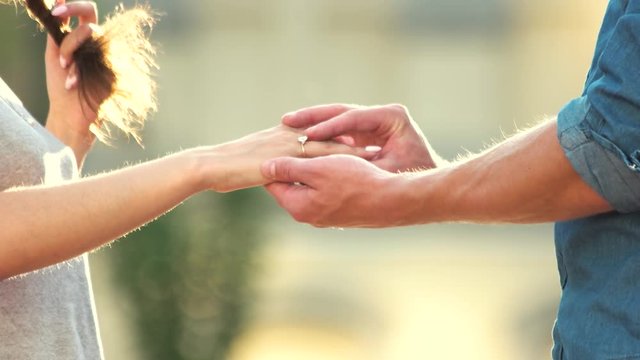 Man putting engagement ring on woman hand outdoors. Young man making marriage proposal to girlfriend. Beautiful sunny day.