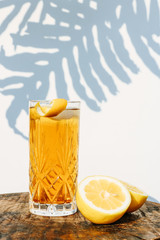 Fresh made ice tea in a cocktail glass standing on a wooden table in front of a white wall  outside with shadows of a palm leaf plant in the background
