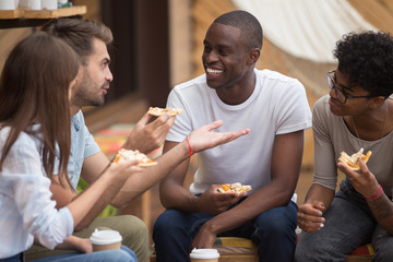 Multiracial happy friends laughing at joke eating pizza in cafe