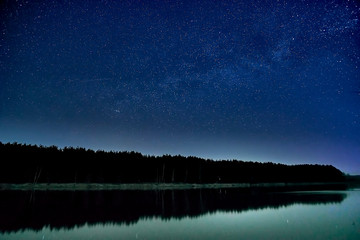 Wonderful beautiful night sky full of stars with Milky way over the river and forest in transparent april night