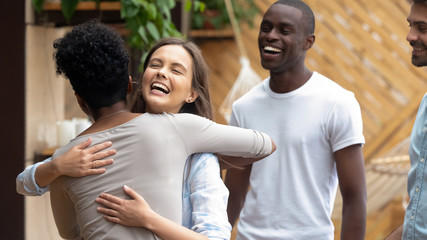 Happy caucasian teen girl embracing african friend at group meeting