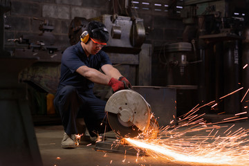 Asian workshop engineer operating an abrasive cut-off saw with metal sparks - Hispanic production technician cutting metal using power tools in a dark factory