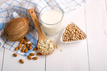 Glass of vegan milk from nuts with various nuts on white wooden table. Lactose free products, different milk substitute, soy, oat, almond, coconut, non-dairy milk alternatives. Top view