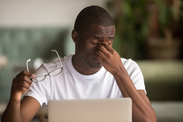 Stressed tired from computer work african man feeling eye strain