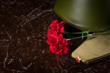 military helmet and cap lie on a monument with red flowers