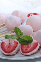 Strawberries in yogurt. Berries are dressed on wooden skewers and dipped in yogurt. Nearby are two halves of dessert. Visible red juicy strawberry flesh. Decorated with mint leaves.