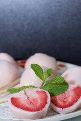Strawberries in yogurt. Berries are dressed on wooden skewers and dipped in yogurt. Nearby are two halves of dessert. Visible red juicy strawberry flesh. Decorated with mint leaves.