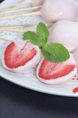 Strawberries in yogurt. Berries are dressed on wooden skewers and dipped in yogurt. Nearby are two halves of dessert. Visible red juicy strawberry flesh. Decorated with mint leaves.