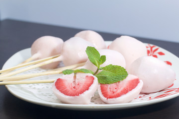 Strawberries in yogurt. Berries are dressed on wooden skewers and dipped in yogurt. Nearby are two halves of dessert. Visible red juicy strawberry flesh. Decorated with mint leaves.