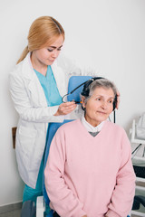 Senior patient wearing headphones, sitting near audiologist during ear exam at hearing clinic