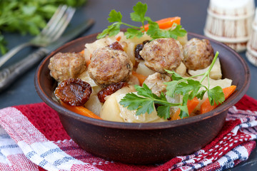 Stewed potatoes with meatballs, carrots and sun-dried tomatoes in a bowl against a dark background