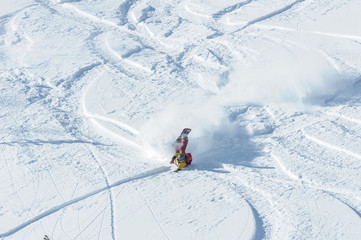 A snowboarder falling into deep snow at the ski resort in a sunny morning