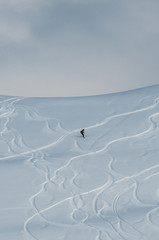 A snowboarder riding down the slope at the ski resort and leaving a smooth track behind
