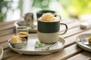 A cup of Hot Coffee with extra shot, sugar cotton candy and with thai traditional snacks on white plate, wood table natural background