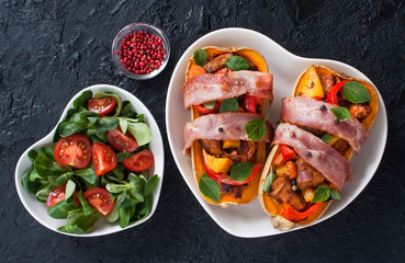 Stuffed pumpkin Butternut meat and vegetables wrapped in bacon and salad on a heart-shaped plate against a black slate background. Top view