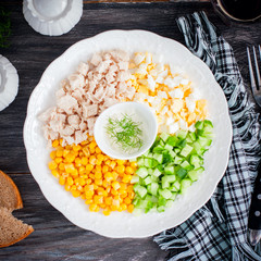 Corn salad, cucumber, egg, chicken on a white plate on a black table, top view, square