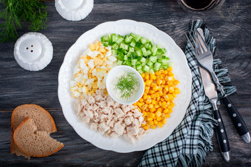 Corn salad, cucumber, egg, chicken on a white plate on a black table, top view, horizontal