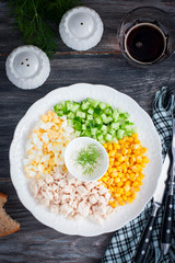 Corn salad, cucumber, egg, chicken on a white plate on a black table, top view, selective focus