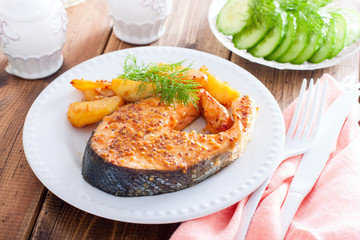 Salmon steak baked with mustard and potatoes on a white plate, horizontal