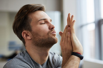 Concentrated serene handsome young man with stubble keeping eyes closed and twisting arms while meditating