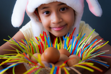 Happy easter! Close up cute girl wearing rabbit hat with chicken eggs in a basket. - 260050336