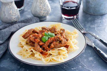 Beef in tomato sauce with farfalle on a white plate, horizontal