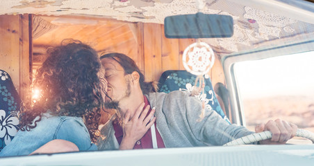 Happy couple kissing inside a vintage mini van - Romantic lovers having a tender moment during a roadtrip - People relationship, vacation, travel and transport concept