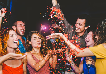Happy friends doing party throwing confetti in the club - Millennial young people having fun celebrating in the nightclub - Nightlife, entertainment and youth festive holidays concept
