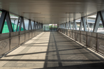 Empty concrete overpass bridge walkway with iron rail and steel roof connect to sky train station with morning sunlight