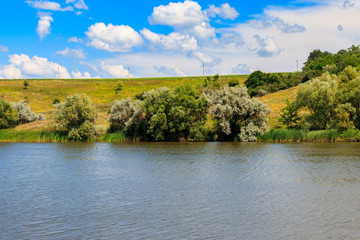 Summer landscape with beautiful lake, green meadows, hills, trees and blue sky
