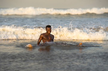 beach portrait of young fit and attractive black African American man with muscular beautiful body enjoying playful in the sea playing on the water having fun