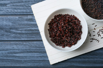 Board with bowls of boiled and uncooked brown rice on table, top view. Space for text