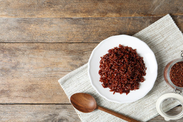 Flat lay composition with plate of boiled brown rice and space for text on wooden background