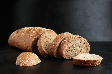 sliced homemade brown rye bread with sesame seeds on black background