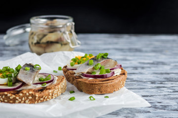 smorrebrod with rye toast bread herring boiling egg chopped green onions on craft paper on rustic wooden table