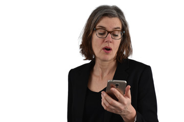 Fototapeta premium Attractive middle-aged woman with half-long graying hair and glasses looks at her phone with a surprised face. White background.