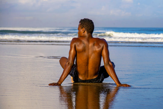 young attractive and relaxed black afro American man with fit body and muscular back sitting on beach sand enjoying beautiful view thinking and meditating free