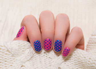 Woman with beautiful nail blue fingernails gracefully crossing her hands to display them to the viewer on a pink background in a fashion, glamour and beauty concept